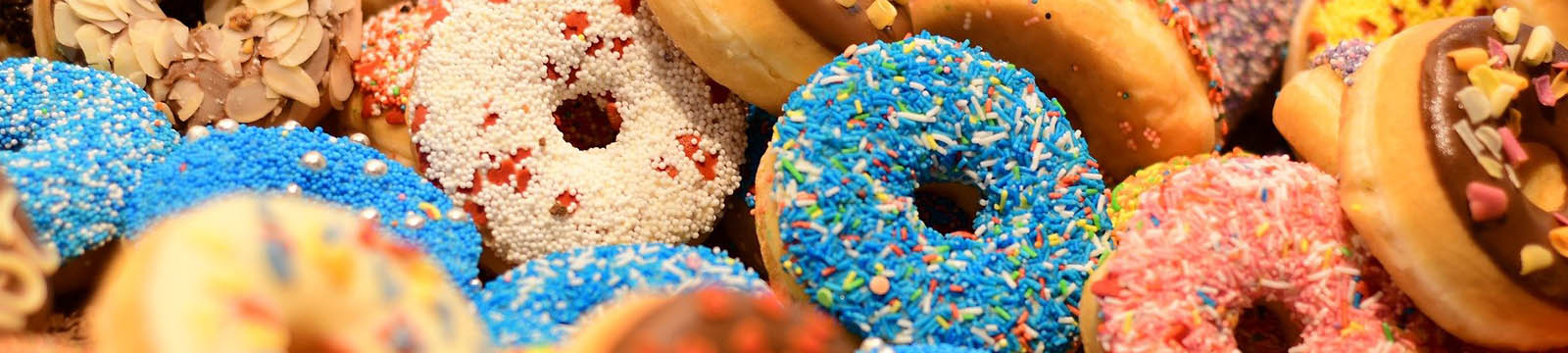 A pile of donuts covered in multi-colored frosting and sprinkles.