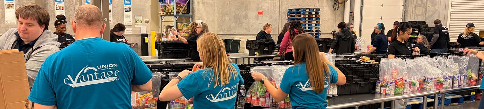 Photo of Union State Bank staff standing with backs to camera working as an assembly line for a food packaging event.