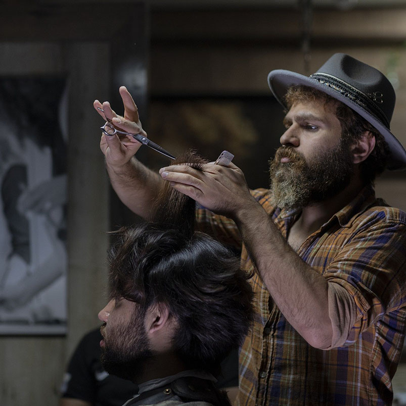 Barber wearing a hat trimming the hair of a client.