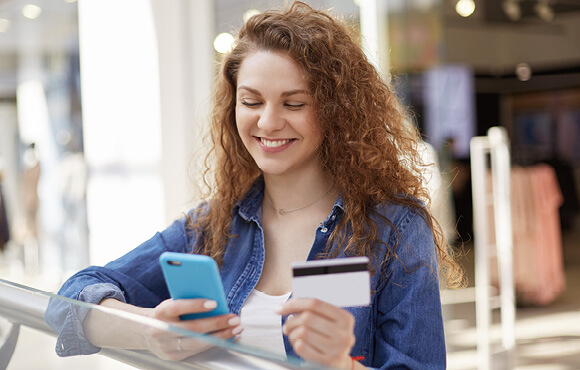 Image of woman holding bank card and mobile phone near store