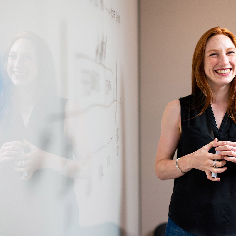 Woman standing in front of a white board with dry erase marker in hand.