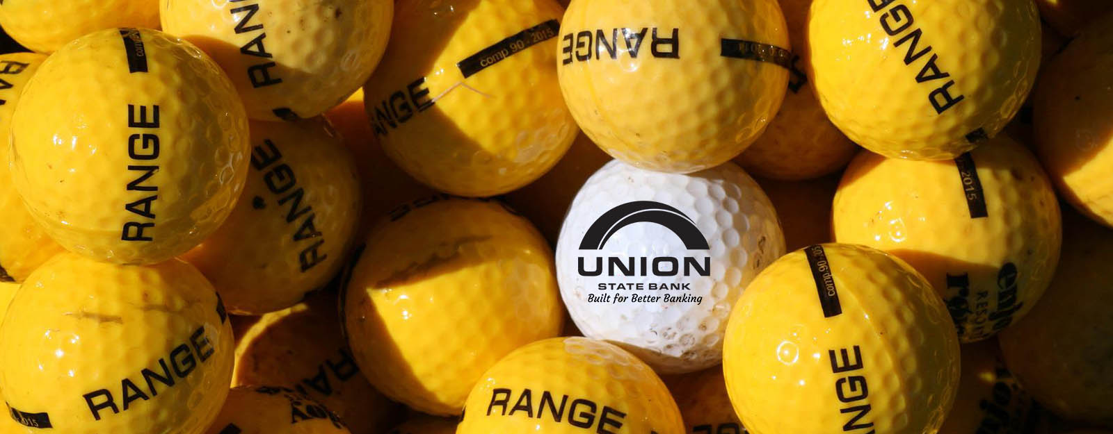 A close up photograph of a pile of yellow golf balls and one white golf ball with the Union State Bank logo in the center.