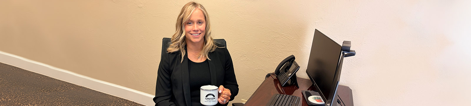 Photo of Taylor Nicks, Director of Mortgage for Union State Bank sitting at a desk holding a coffee mug.