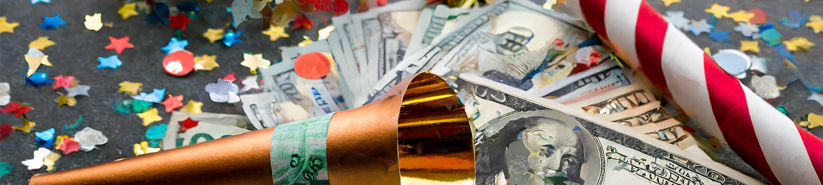 Photo of a party horn and confetti lying on top of a pile of one-hundred dollar bills.