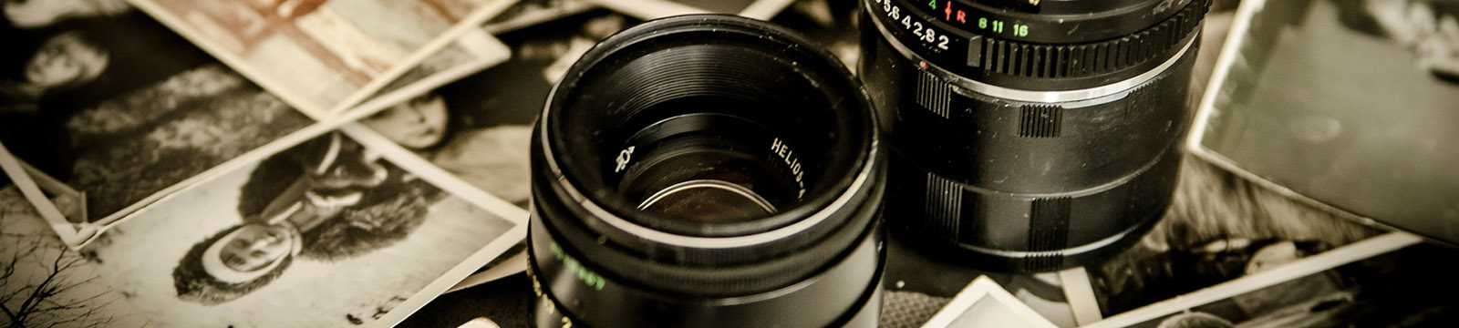 Photo of camera lens on top of a stack of scattered photographs.