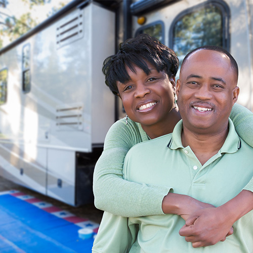 An older couple poses in front of a large RV.