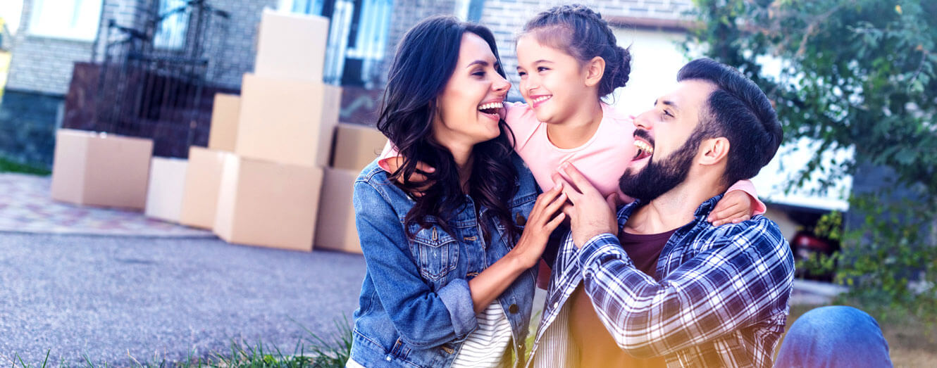 Image of man and woman holding up child in front of house