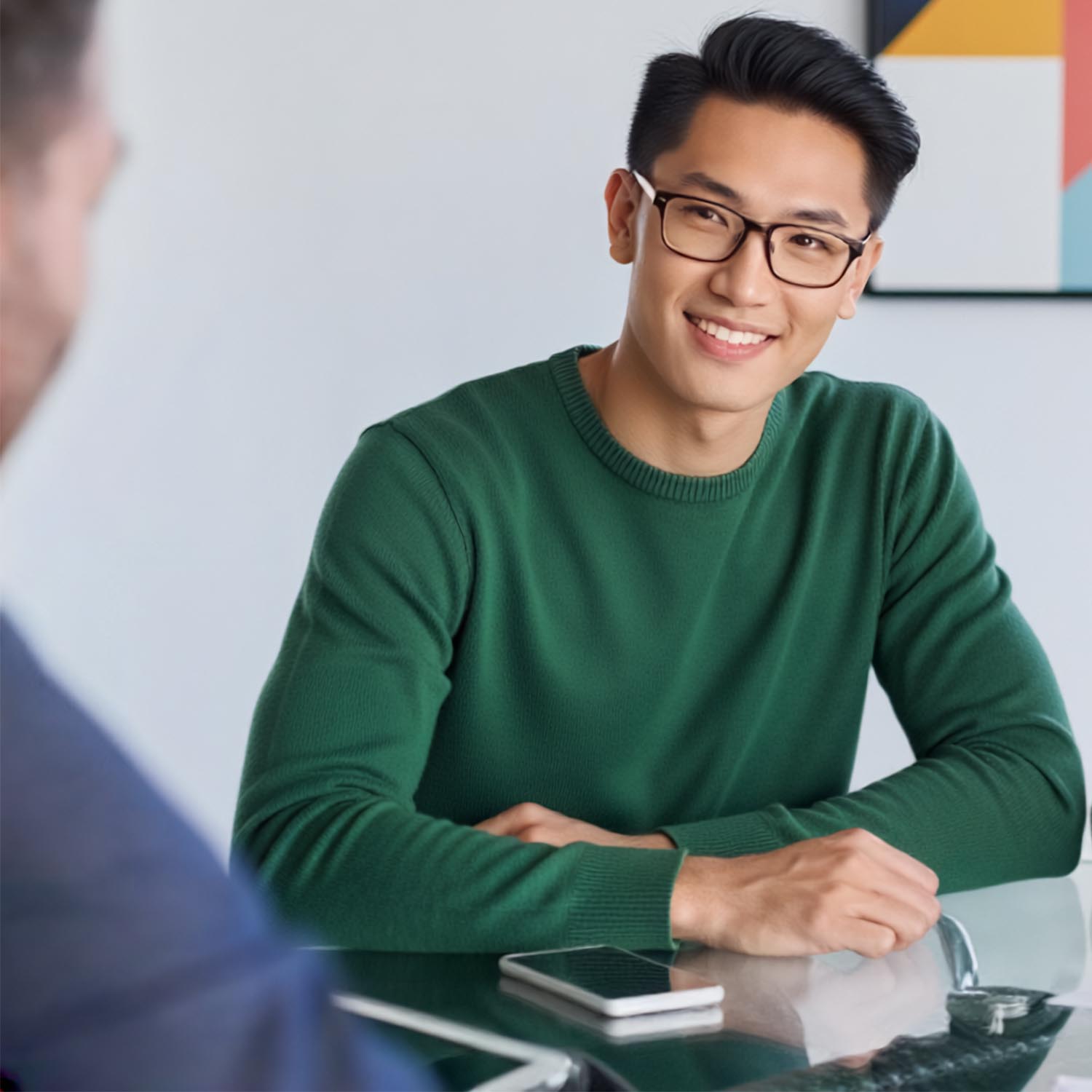 Image of a young adult sitting in an office and facing towards another person.