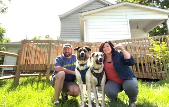 Photo of the Mugler family in front of their new home with their dogs.