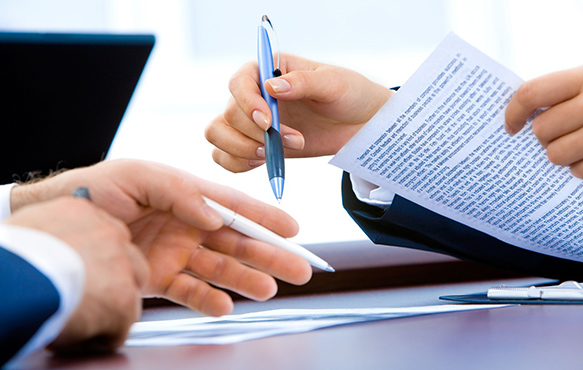 Close up photo showing the hands of two people holding pens and going over a document.
