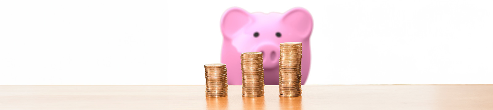 Photo of coins stacked with a piggy bank in the background.