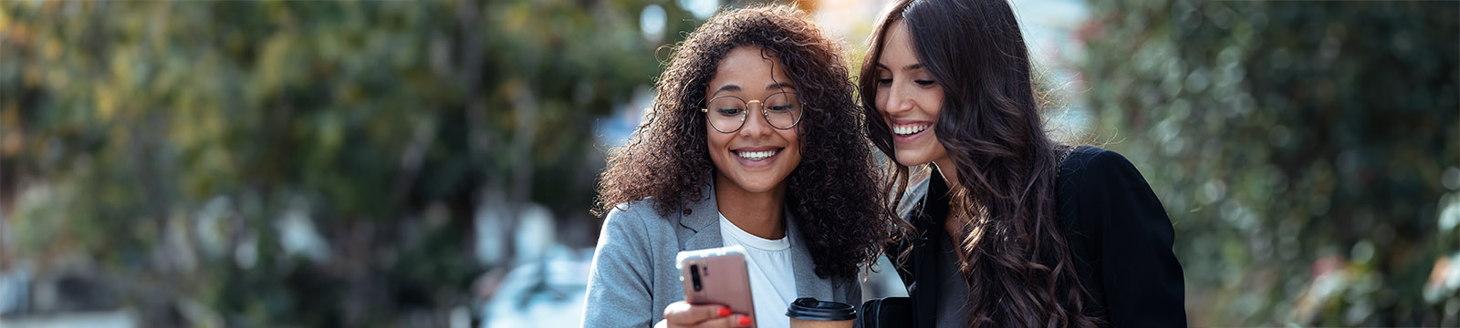 Photo of two women in an outdoor urban setting looking at a cell phone that one is holding.