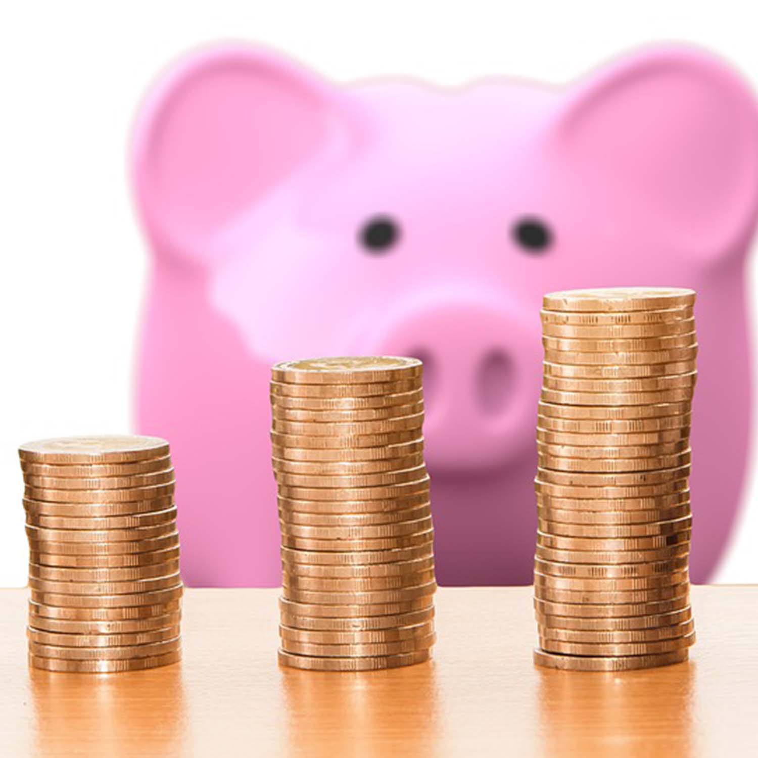 Photo of three stacks of coins with a piggy bank in the background.