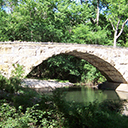 Photo of a stone bridge spanning over a body of water with trees in the background.
