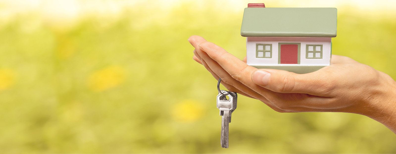 Photo of hand holding a model house in open palm with keys hanging off of a finger.