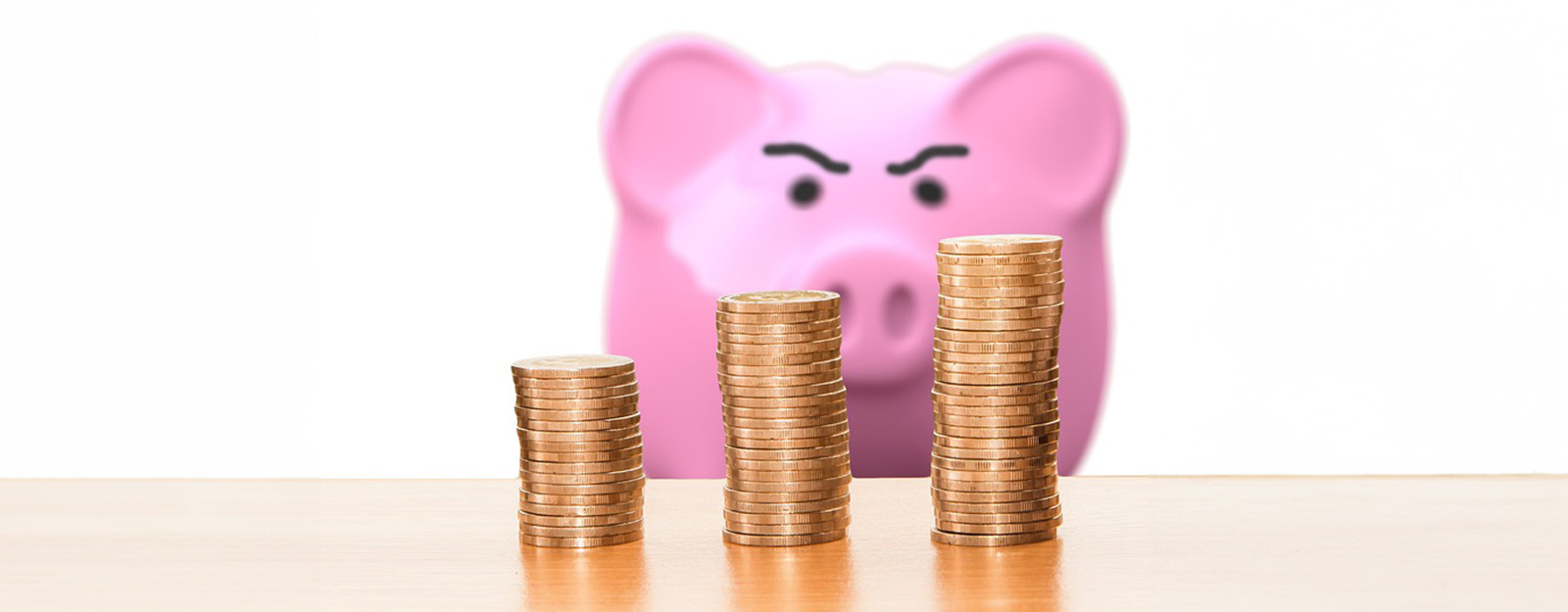 Photo of coins stacked with an angry looking piggy bank in the background.