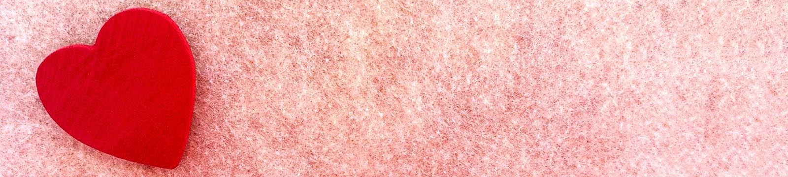 Image of a red felt heart on a pink background.