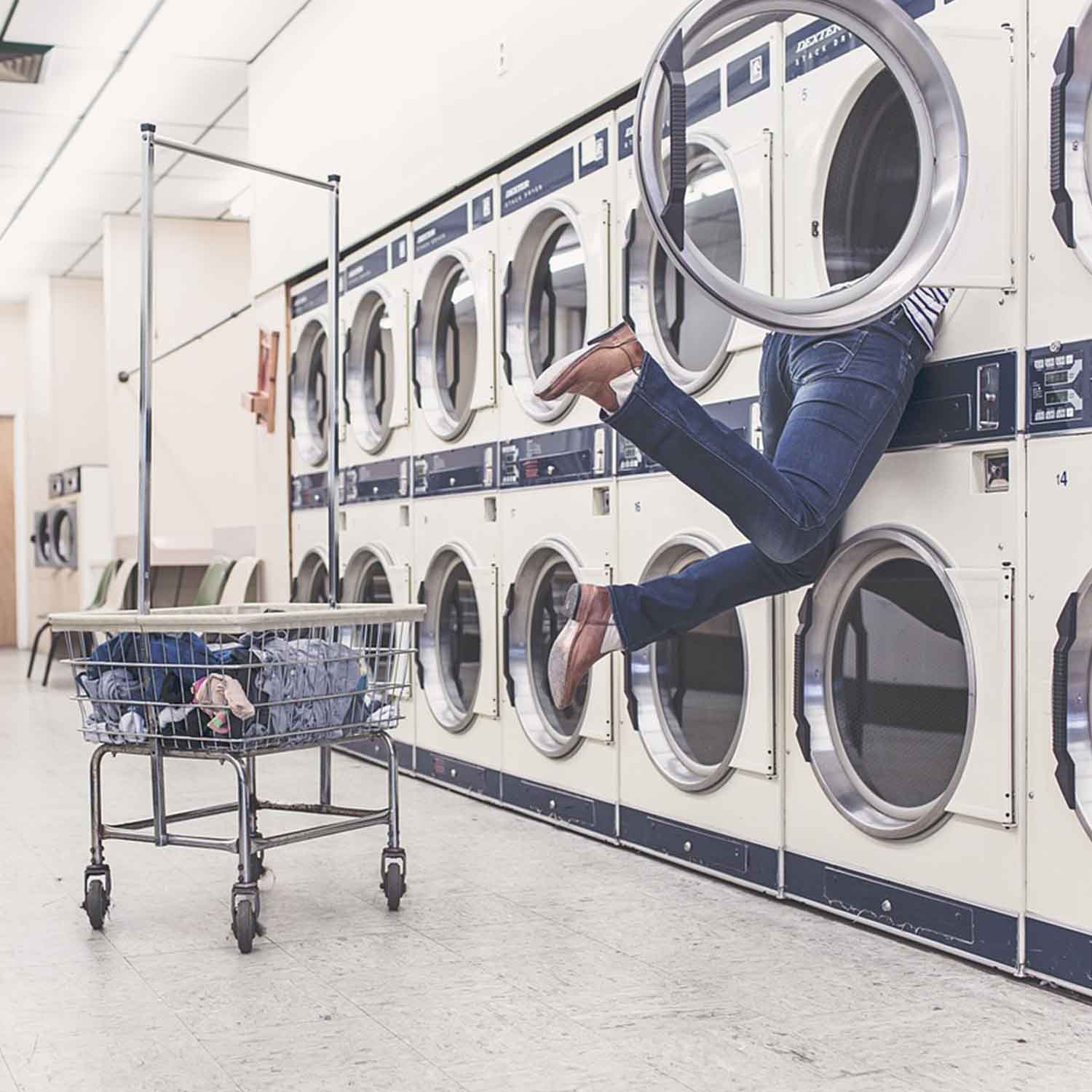 Photo of a young woman partially inside of a laundromat dryer.