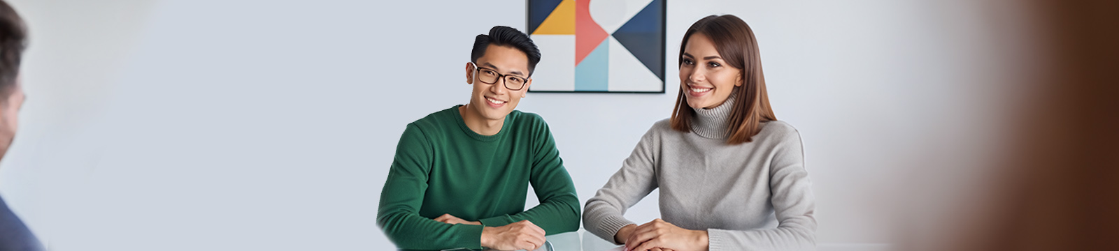 Image of a young adult couple sitting at a table facing towards another person.