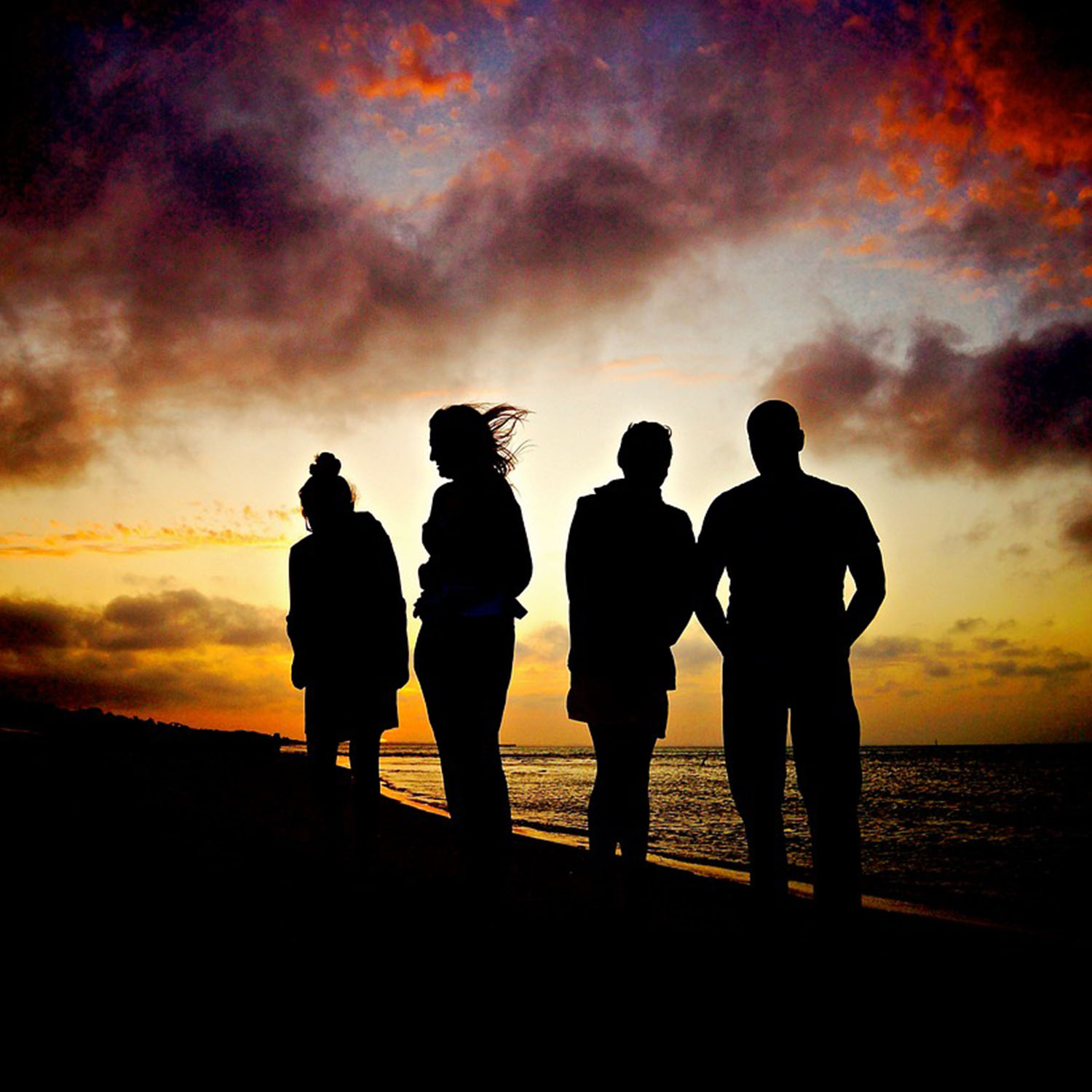 Photograph of young adults standing on a shoreline looking into a sunset.