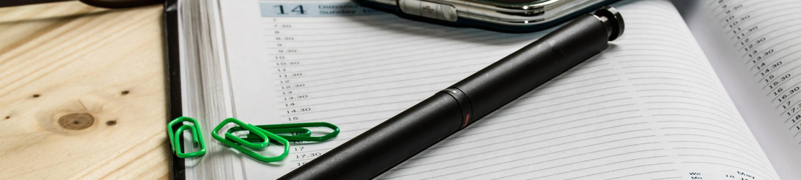 Photo of a desktop calendar open with a pen, paperclips and cellphone on top.